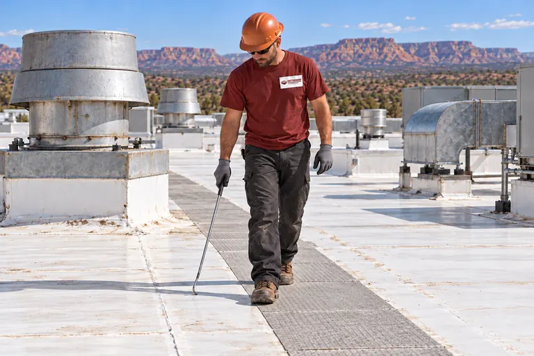 Roofer walking a walkway-pad path past exhaust fans on an industrial roof