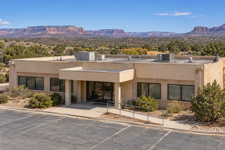 Single-story tan stucco commercial building with a low-slope roof and rooftop units, red-rock mesas behind